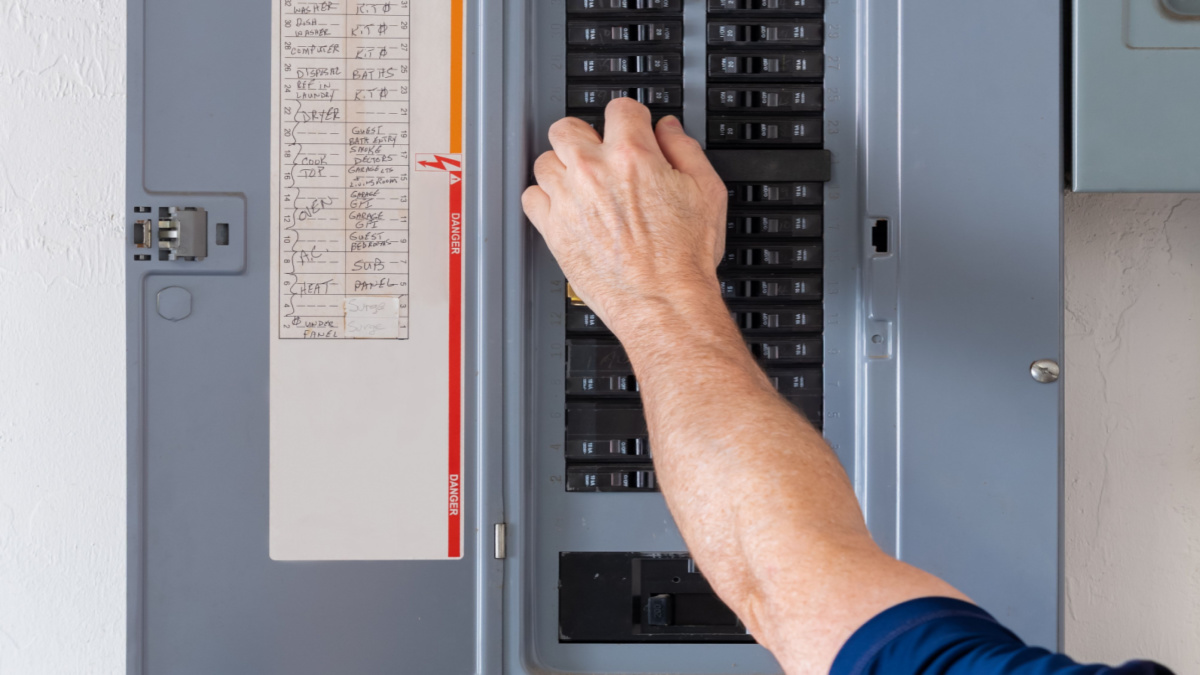 A man's arm and hand reaching for a circuit breaker in a residential electrical panel
